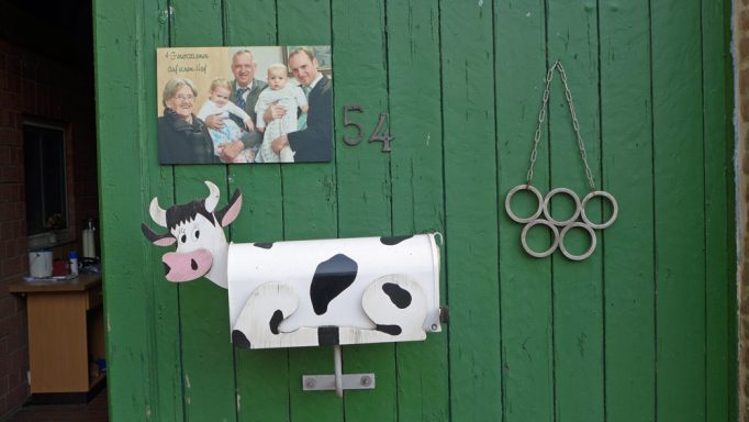 Grüne Holztür mit einer Kuhskulptur, einem Olympiaring-Symbol und einem Schild.