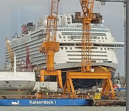 Großer Kreuzfahrtschiff im Hafen, umgeben von Kränen und Baustellen.