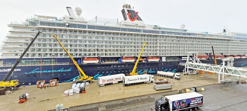 Großer Kreuzfahrtschiff am Kai mit Frachtwagen und unbeständigem Wetter.