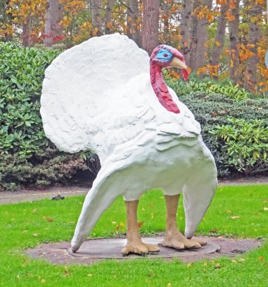 Große weiße Skulptur eines Truthahns in einem Park mit Bäumen im Hintergrund.