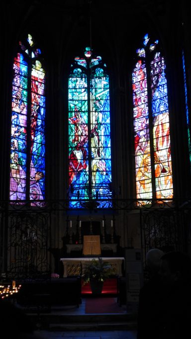 Bunt verglaste Kirchenfenster mit biblischen Szenen, beleuchtet von innen.