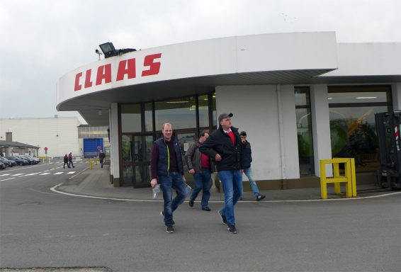 Zwei Männer gehen an einem Claas-Gebäude vorbei. Dunkler Himmel im Hintergrund.