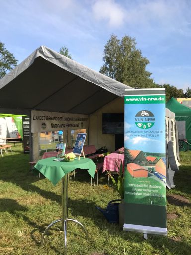 Ein Zeltausschnitt mit Tisch, Bannern und Displays auf einer Wiese.