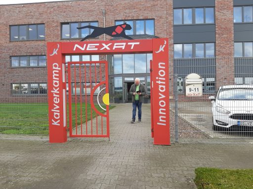 Roter Eingang mit dem Schriftzug "NEXAT" und einem Mann vor einem modernen Gebäude.