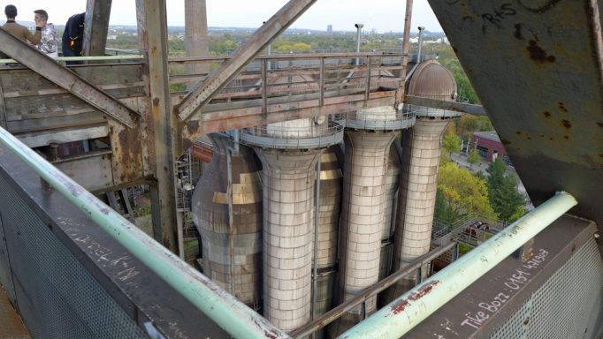 Drei große Röhren in einem rustikalen Industriegebäude, umgeben von Grün.