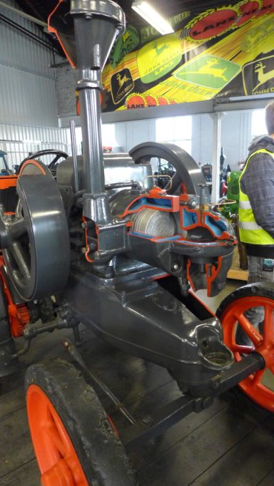 Dampfpflug mit schwarzen und orangefarbenen Komponenten in einer Ausstellungshalle.