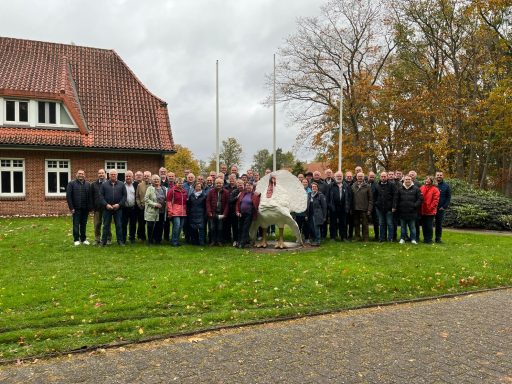 Gruppenfoto von Teilnehmern vor einem Gebäude mit Skulptur im Freien, herbstliche Umgebung.