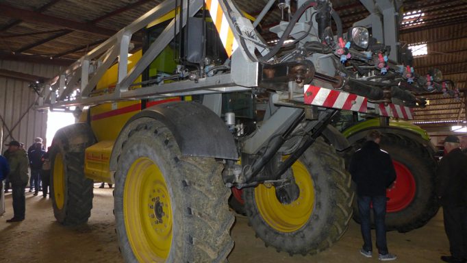 Ein großer Traktor mit gelben und grauen Farben in einer Halle, umgeben von Menschen.