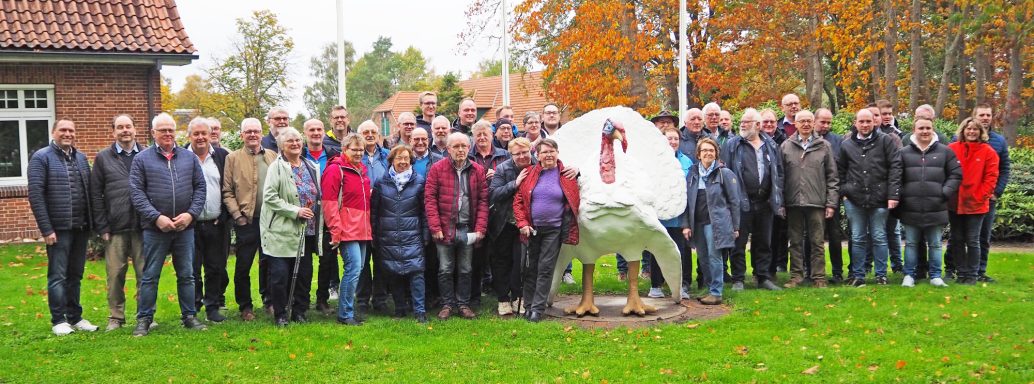 Gruppenfoto mit vielen Personen, die auf einem grünen Rasen stehen, hinter einer Statue.