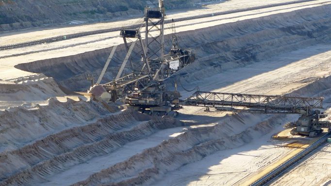 Großes Maschinenbaugerät in einem Tagebau, umgeben von Erdaushub und Sonnenlicht.