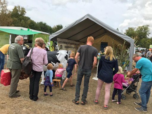 Menschen auf einem Fest, Kinder und Erwachsene stehen vor einer Bühne und einem Bauernhof.