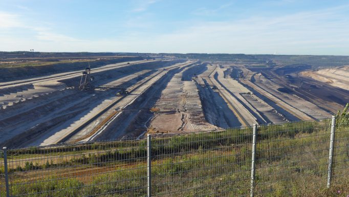 Großes Tagebaugebiet mit geordneten Erdschichten und Baggern im Hintergrund unter blauem Himmel.