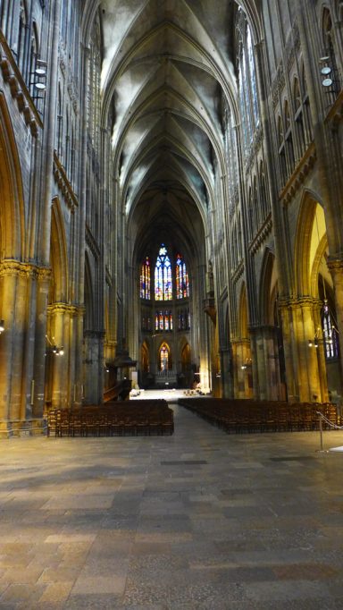 Hohe gotische Kirchenarchitektur mit beleuchteten Säulen und bunten Fenstern.