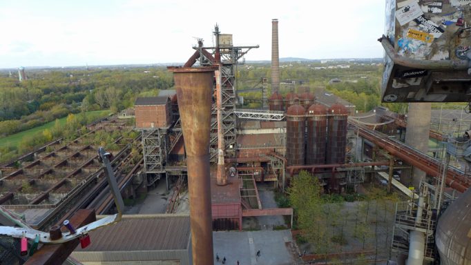 Industrielandschaft mit alten Hochöfen und Werkstätten, umgeben von Grünflächen.