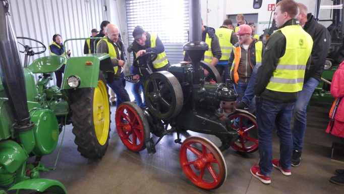 Historische Maschinen und Traktoren in einer Halle, umringt von Besuchern in Warnwesten.