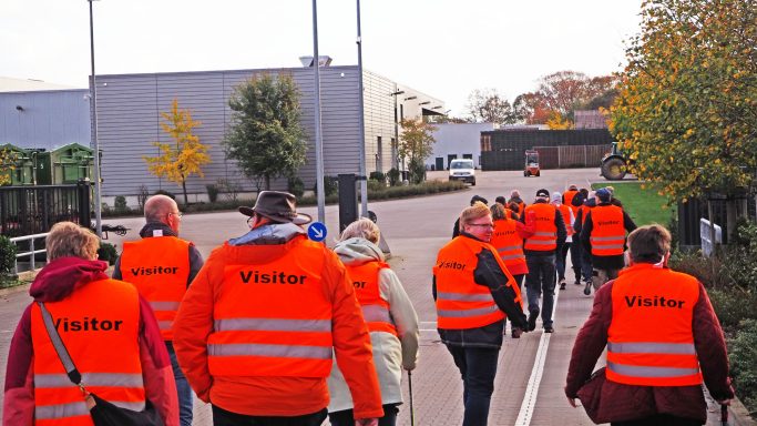 Gruppe von Menschen in orangefarbenen Weste, die eine Straße entlanggehen.
