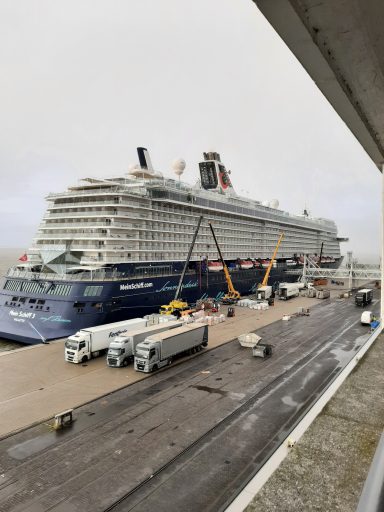 Ein großes Kreuzfahrtschiff liegt im Hafen, umgeben von Baustellen und Fahrzeugen.