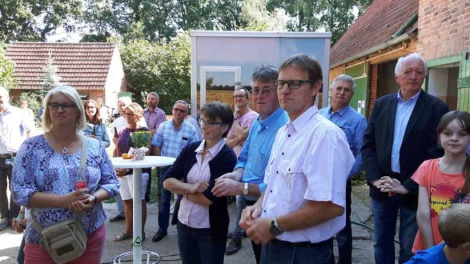 Gruppe von Menschen, die in einem Garten stehen und aufmerksam einer Ansprache lauschen.